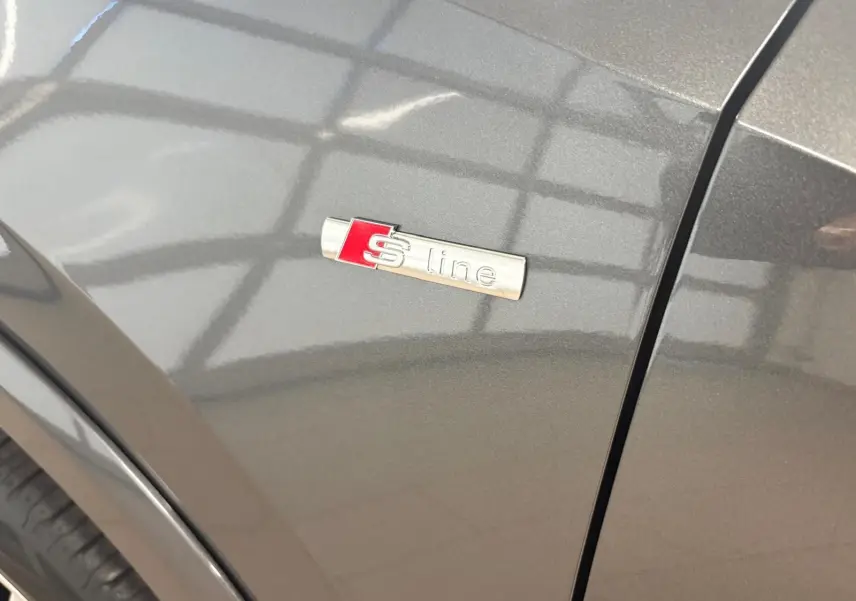 Gros plan sur l'emblème S line sur l'aile avant droite d'un Audi Q2 gris Daytona métallisé.