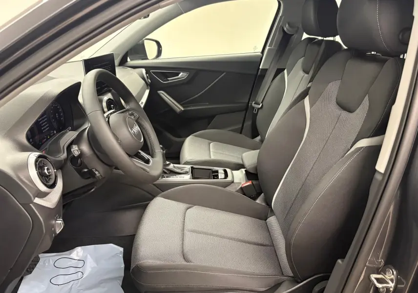 Vue intérieure côté conducteur de l'Audi Q2 35 TFSI S Line 2026, sièges tissu gris et tableau de bord moderne.