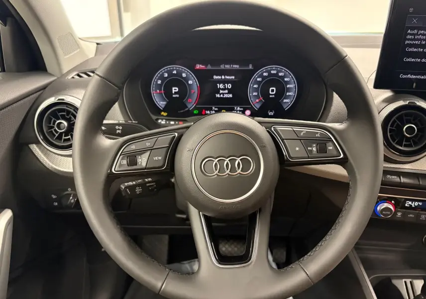 Vue intérieure centrée sur le volant noir de l'Audi Q2 35 TFSI S Line avec tableau de bord digital et aérateurs ronds.