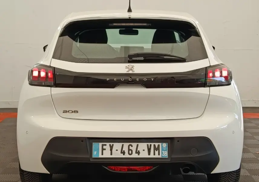 Vue arrière d'une Peugeot 208 blanche avec feux arrière allumés et bande noire distinctive entre les feux.