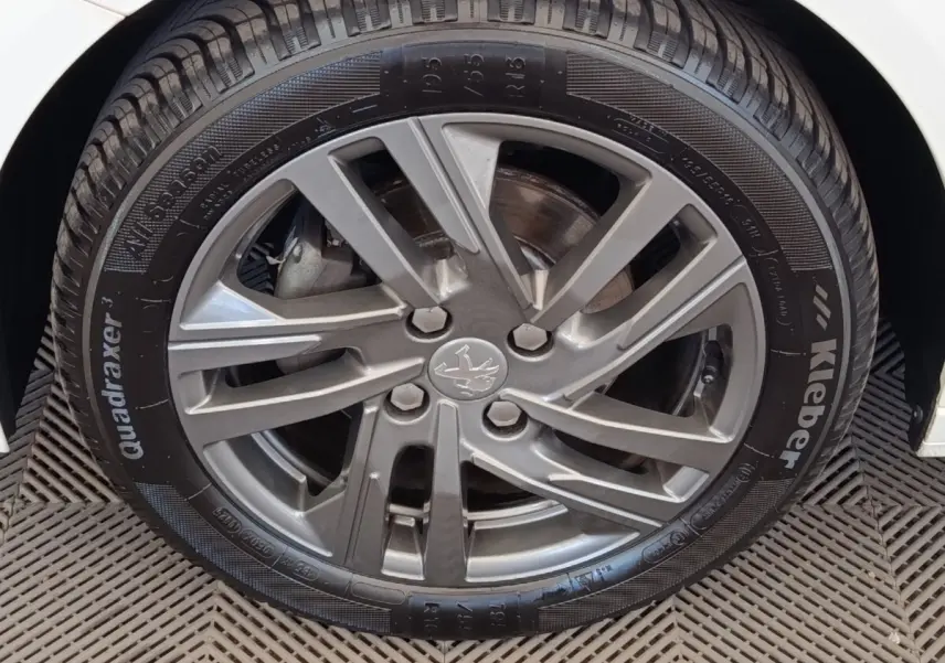Gros plan sur la roue avant droite d'une Peugeot 208 blanche, mettant en valeur la jante alliage grise et le pneu Kleber.