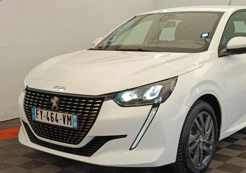 Vue 3/4 avant droit d'une Peugeot 208 blanche de 2021 avec phares LED allumés et calandre noire distinctive.
