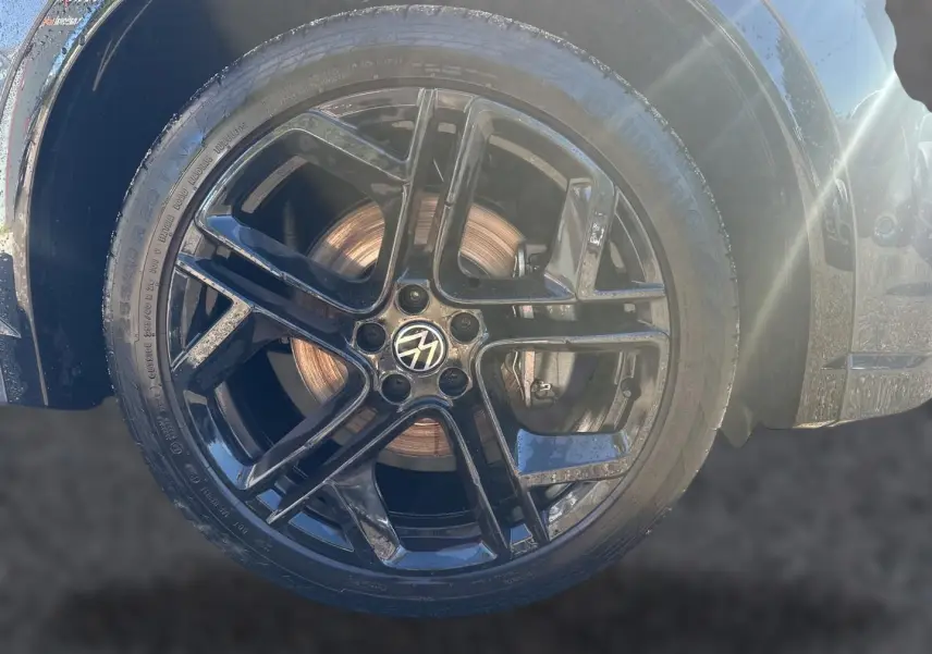 Gros plan sur la jante alu noire brillante avec logo Volkswagen d’un Volkswagen Tiguan gris dauphin.