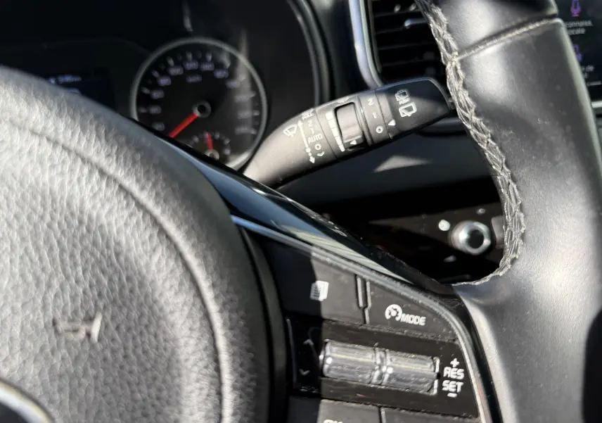 Gros plan sur le volant côté gauche du Kia Sportage bleu 2021, avec commandes de régulateur de vitesse visibles.