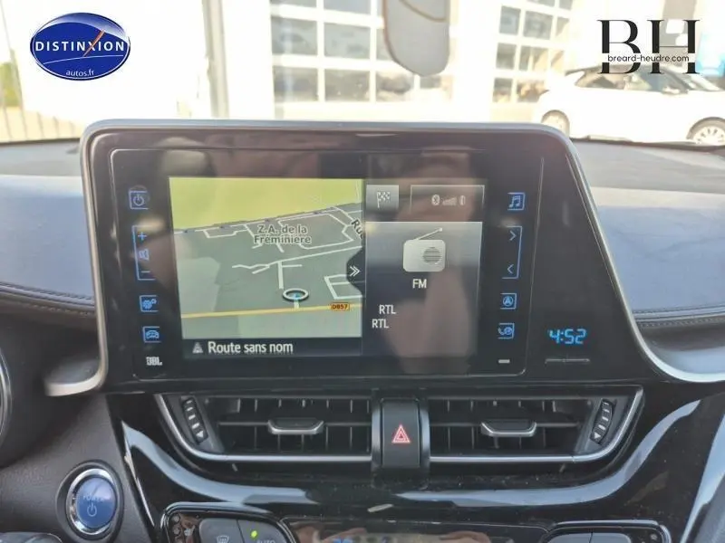 Écran tactile central du Toyota C-HR gris aluminium 2019 affichant navigation et radio FM, avec commandes et aérateurs visibles.
