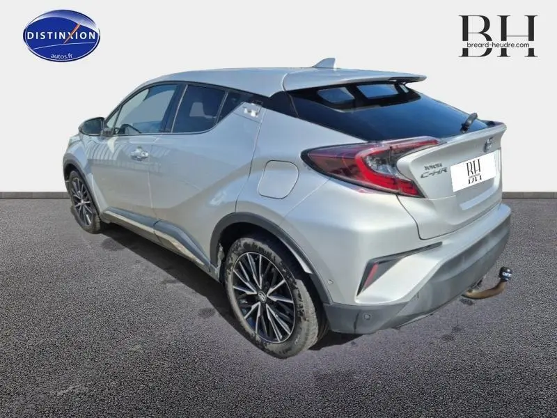 Vue 3/4 arrière droite d'un Toyota C-HR 122h Distinctive gris aluminium avec jantes alliage et toit noir sur fond neutre.