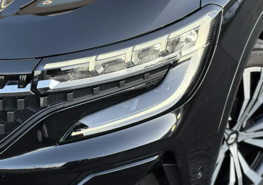 Gros plan sur le phare avant droit et la calandre noire étoilée du Renault Austral 2023 noir Étoile.