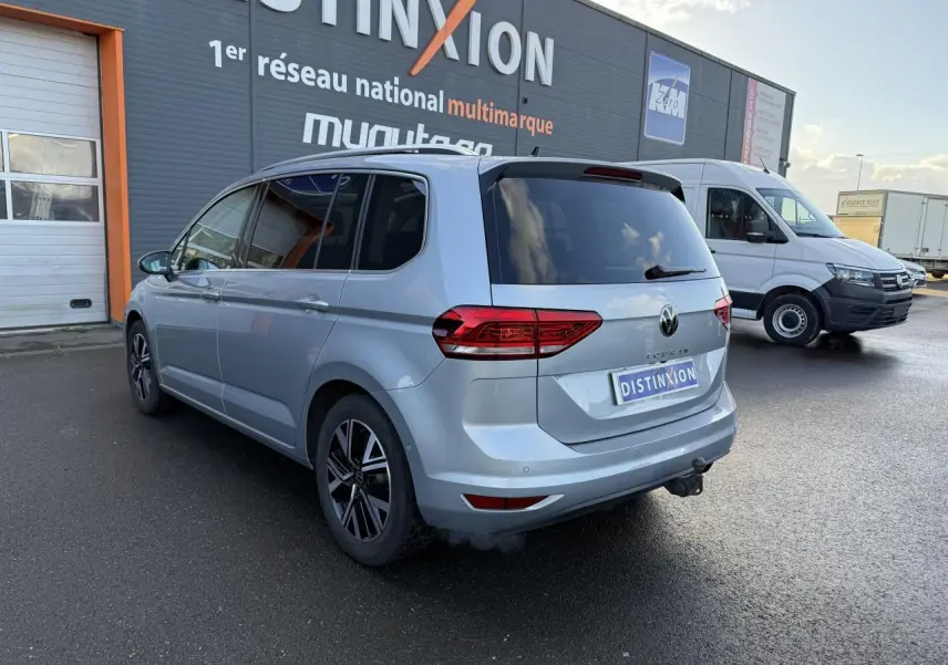 Vue 3/4 arrière droite d'un Volkswagen Touran argent Dolomite avec jantes alliage et attelage visible sur parking.