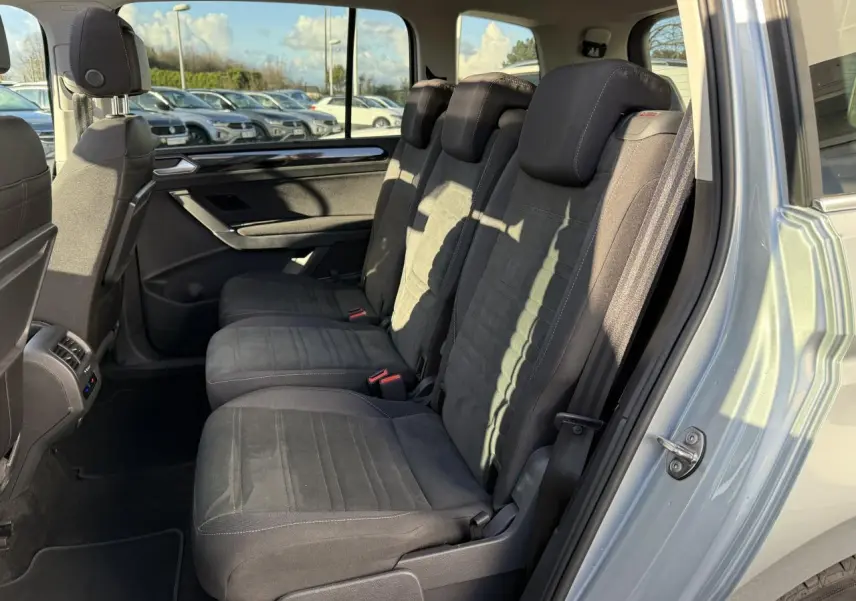 Vue côté droit sur les sièges arrière noirs en microfleece d'un Volkswagen Touran argent Dolomite 2025 avec porte ouverte.