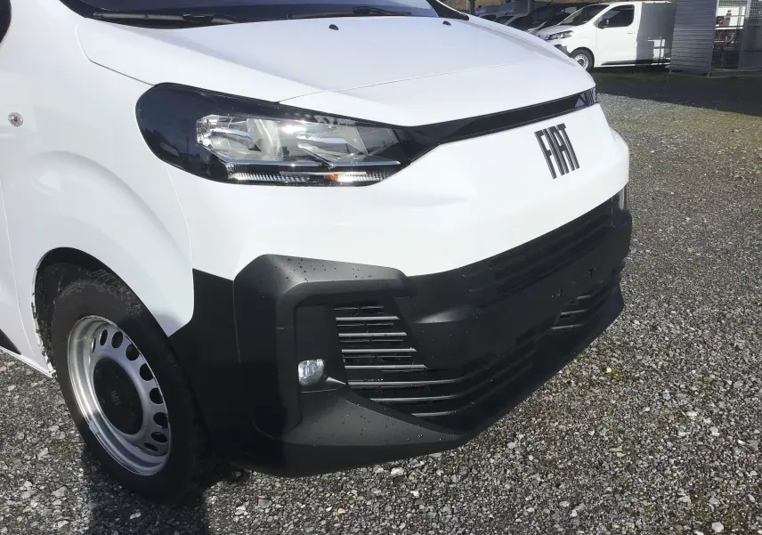 Vue 3/4 avant gauche d’un FIAT Scudo Fourgon blanc 2024 avec pare-chocs noir et jante acier sur sol gravillonné.