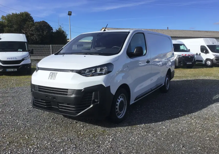 Fiat Scudo Fourgon blanc vu en 3/4 avant droit, avec pare-chocs noir et garde au sol rehaussée sur terrain gravillonné.