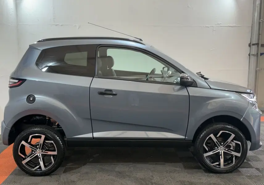 Vue de profil côté gauche de l'AIXAM AMBITION 0.5 CROSSOVER PREMIUM gris foncé avec jantes alliage et caméra rétro côté conducteur.
