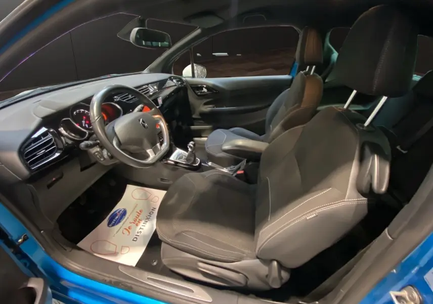 Vue intérieure côté conducteur d'une Citroën DS3 bleu avec toit blanc, sièges noirs et volant multifonction.