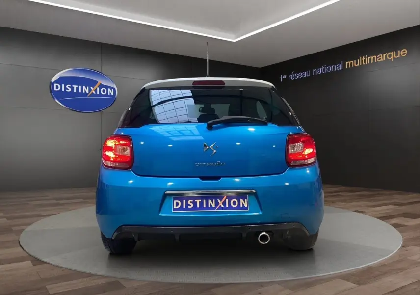 Vue arrière d'une Citroën DS3 bleu avec toit blanc, feux allumés et sortie d'échappement chromée visible.