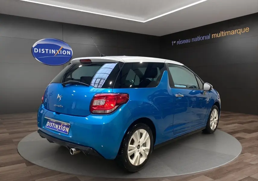 Citroën DS3 bleu avec toit blanc, vue 3/4 arrière droit, sur plateau intérieur avec logo Distinxion.