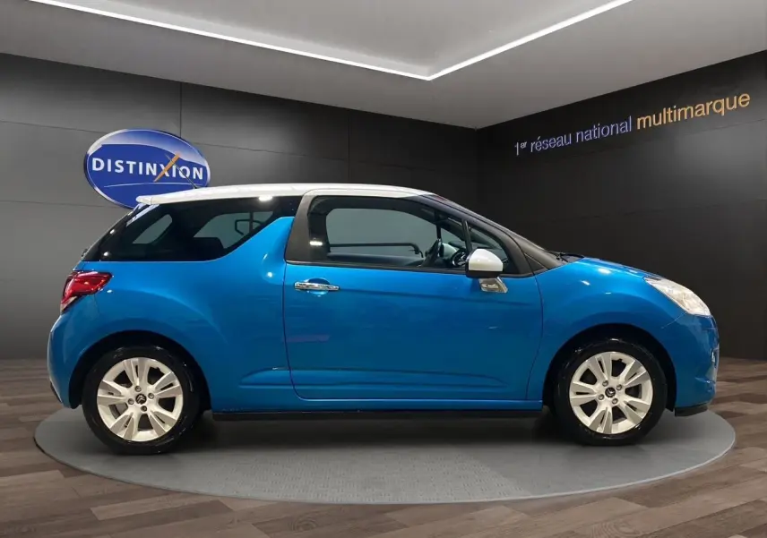 Profil droit d'une Citroën DS3 bleu avec toit blanc, jantes alliage et rétroviseurs blancs, en présentation showroom.