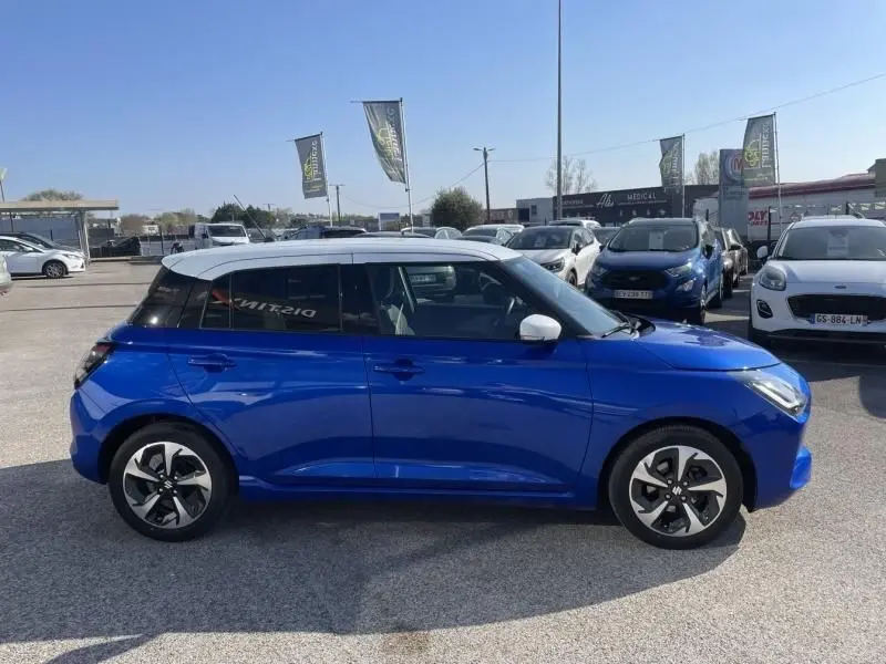 Suzuki Swift 2024 bleu métal vue de profil côté gauche, toit blanc contrasté et jantes au design moderne.
