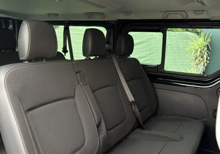 Vue intérieure latérale droite des sièges noirs du Nissan Primastar Combi L2 3T 2025 avec vitres coulissantes ouvertes.