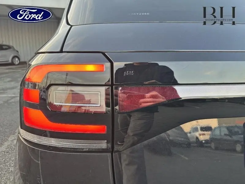 Feu arrière gauche allumé d'un Volkswagen T-cross noir intense nacré, vue rapprochée du coffre et du feu.