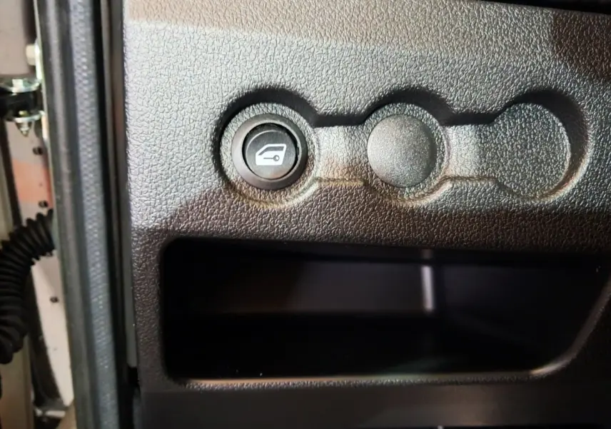 Détail intérieur montrant le bouton d'ouverture du coffre sur la portière côté conducteur d'une Aixam Ambition blanche.