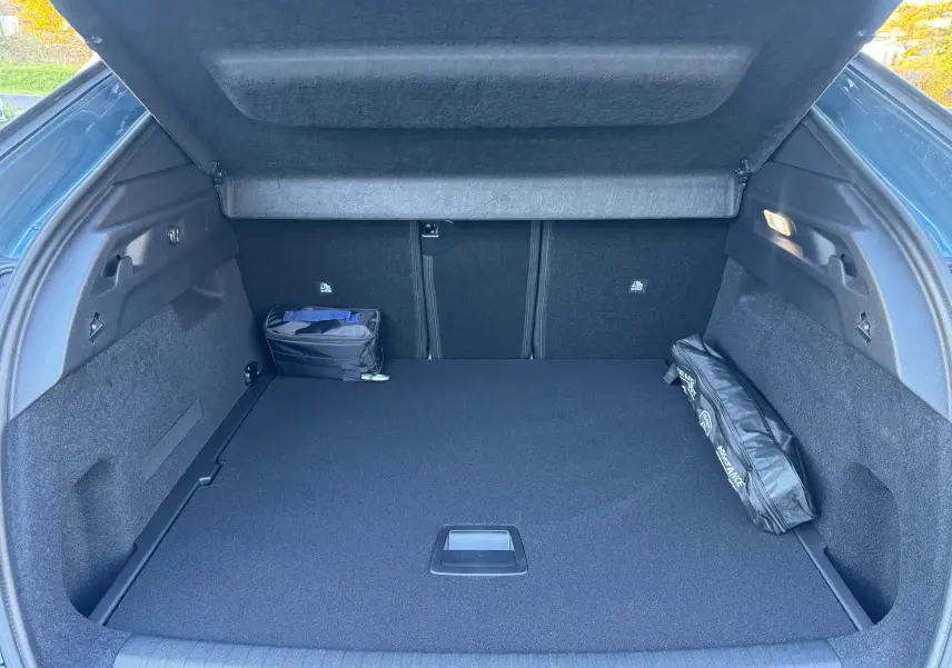 Vue intérieure du coffre ouvert du Peugeot 3008 Hybrid 136ch Allure bleu Nogaro, avec tapis noir et rangement latéral.