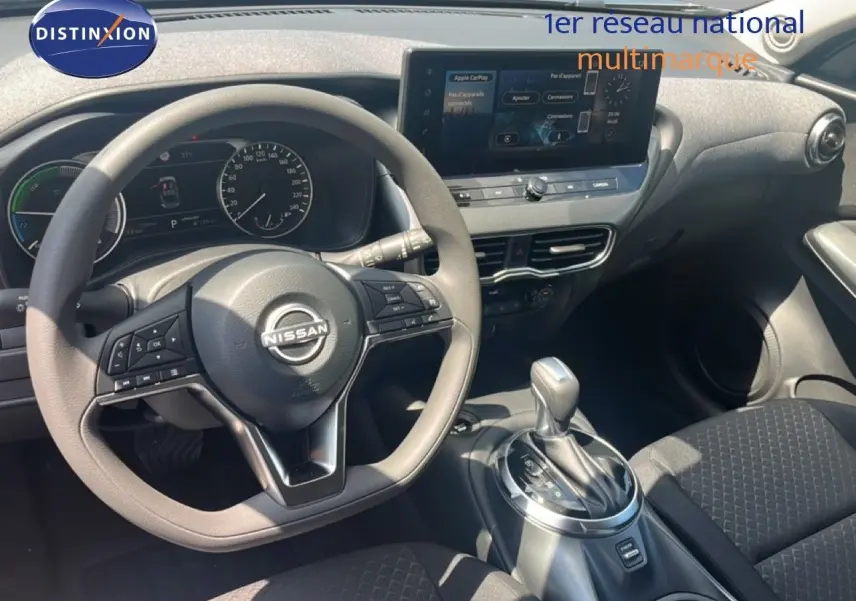 Vue intérieure du poste de conduite du Nissan Juke Hybrid 2025, volant multifonction et écran tactile central visibles.