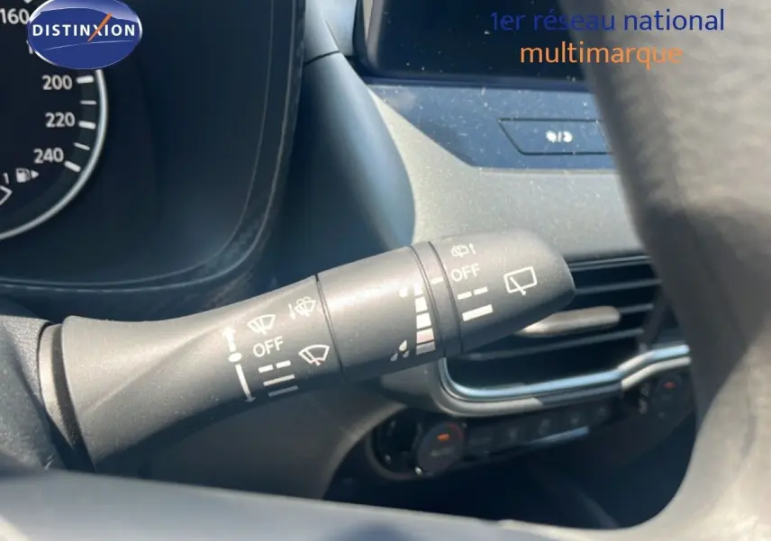 Gros plan sur la commande d’essuie-glace à gauche du volant du Nissan Juke gris, avec tableau de bord et écran tactile en arrière-plan.