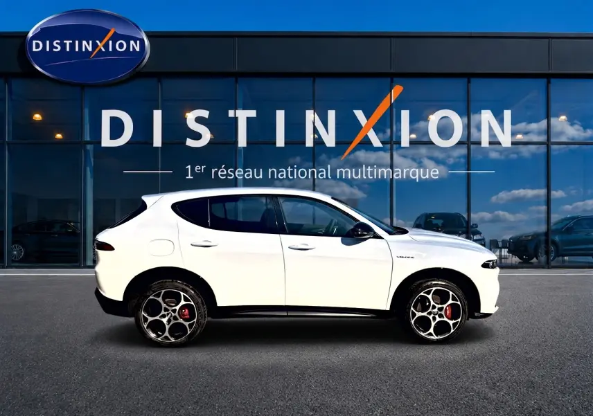 Profil droit d'un Alfa Romeo Tonale blanc 2025 avec jantes alu distinctives, devant une vitrine Distinxion.