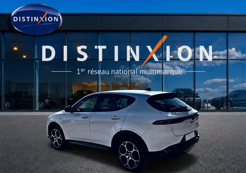 Vue 3/4 arrière droite d'une Alfa Romeo Tonale blanche 2025 avec jantes alu et becquet arrière noir devant un showroom Distinxion.