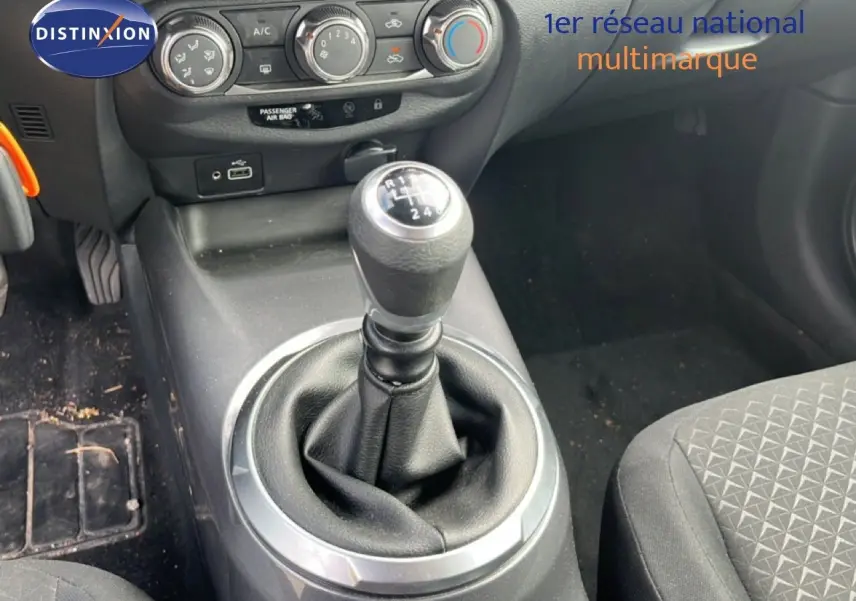 Gros plan sur la console centrale du Nissan Juke 2023 noir métal, avec levier de vitesse manuel et commandes de climatisation.