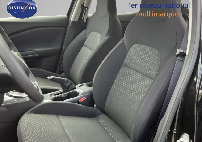 Vue intérieure côté conducteur du Nissan Juke 2023 montrant les sièges en tissu gris et la console centrale noire.