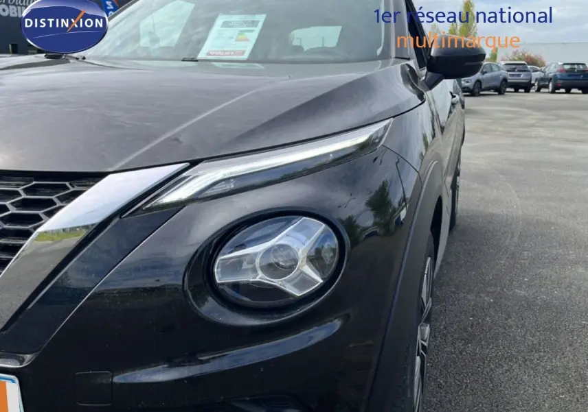 Gros plan sur l'avant droit du Nissan Juke noir métal 2023, mettant en valeur son phare rond et sa calandre hexagonale.