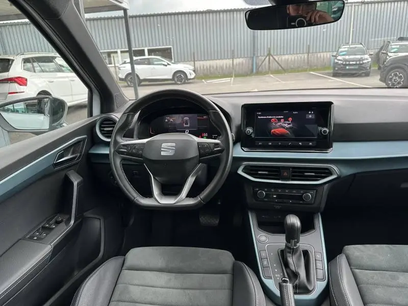 Vue intérieure avant du SEAT Arona 2025, tableau de bord avec volant cuir multifonction et écran tactile central.
