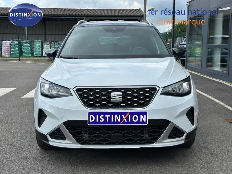 Vue frontale d'un SEAT Arona blanc Nevada avec toit noir Minuit, calandre noire et phares LED allumés.
