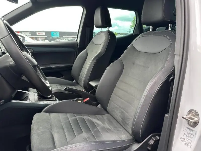 Vue intérieure côté conducteur du SEAT Arona 2025 blanc Nevada, sièges tissu gris Sano avec surpiqûres blanches.