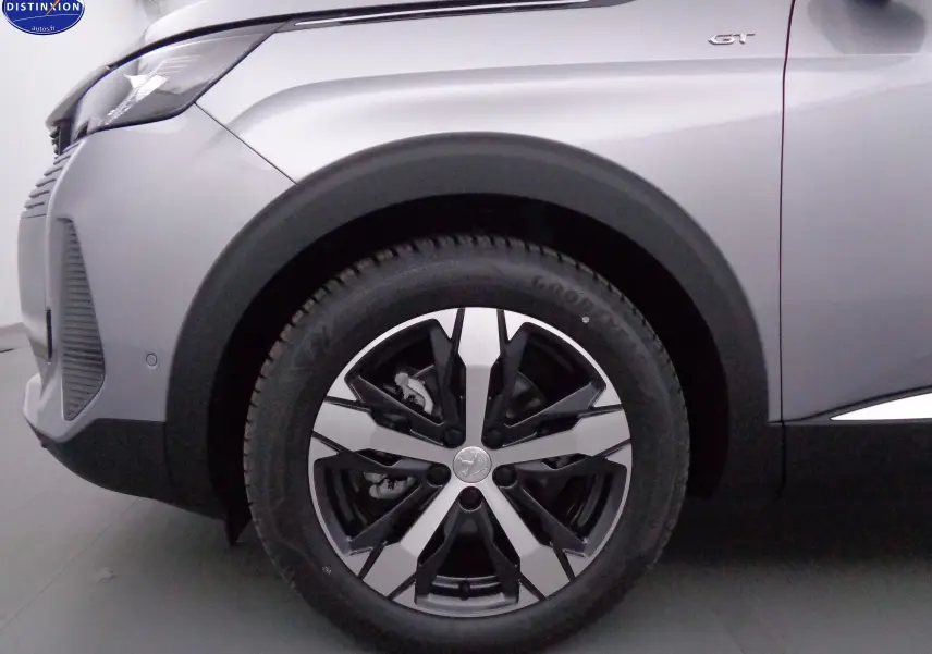 Gros plan sur la roue avant gauche et l'aile gris artense métallisé du Peugeot 3008 GT 2023 avec logo GT visible.
