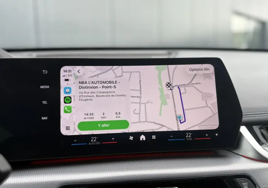 Écran tactile incurvé du tableau de bord du BMW X1 blanc Mineral, affichant la navigation GPS en cours.