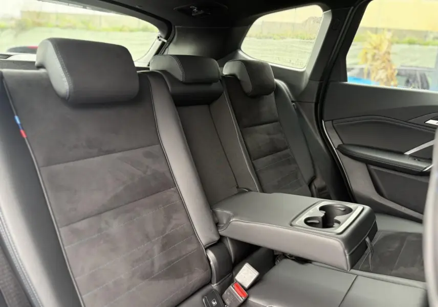 Vue intérieure arrière côté droit montrant les sièges Alcantara noirs avec accoudoir central et porte-gobelets du BMW X1 2025.