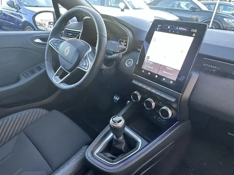 Vue intérieure côté conducteur de la Renault Clio V 1.0 TCE 90 Esprit Alpine 2025, avec volant, écran tactile vertical et levier de vitesse manuel.