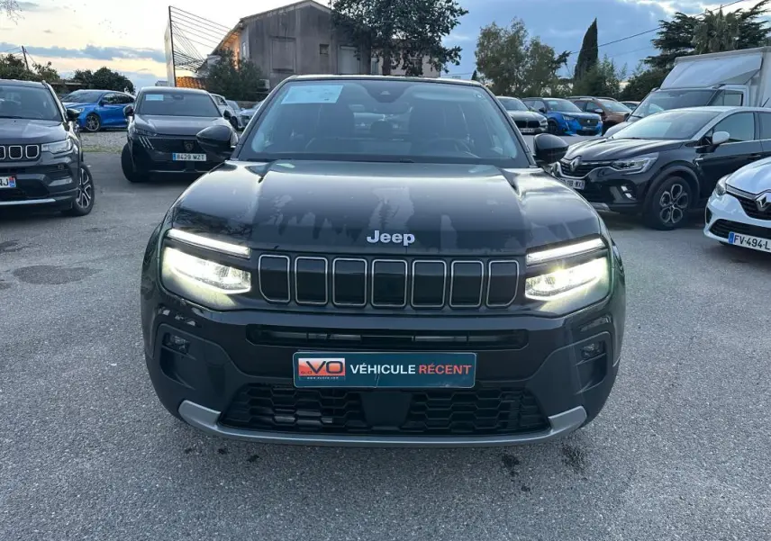 Vue avant frontale du Jeep Avenger noir 2025 avec phares LED allumés et calandre caractéristique à sept fentes.