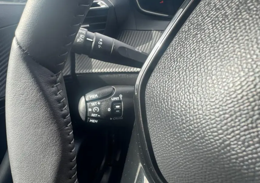 Gros plan sur la commande de régulateur de vitesse à gauche du volant en cuir noir du Peugeot 2008 blanc 2024.