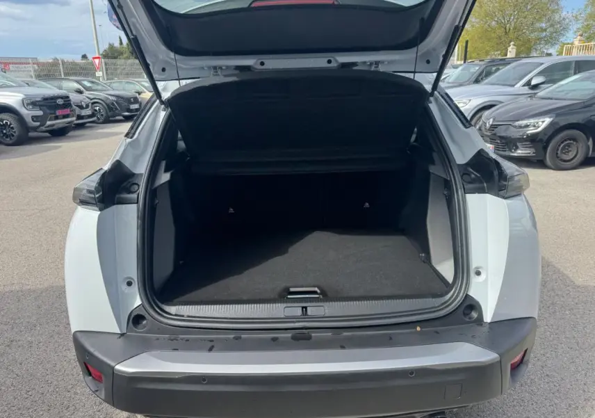 Coffre ouvert vu de l'arrière d'un Peugeot 2008 blanc 2024 avec barres de toit et jantes alliage 17 pouces.