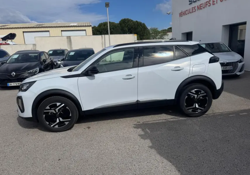 Peugeot 2008 blanc vue de profil côté gauche, avec jantes alliage noires et barres de toit visibles.