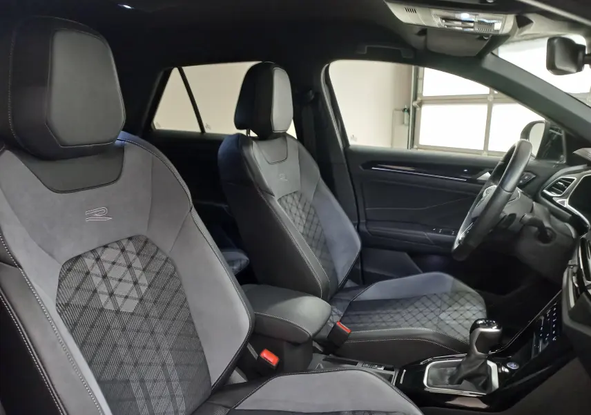 Vue intérieure côté conducteur du Volkswagen T-Roc 1.5 TSI R-Line 2025, sièges sport en tissu et alcantara gris avec logo R.