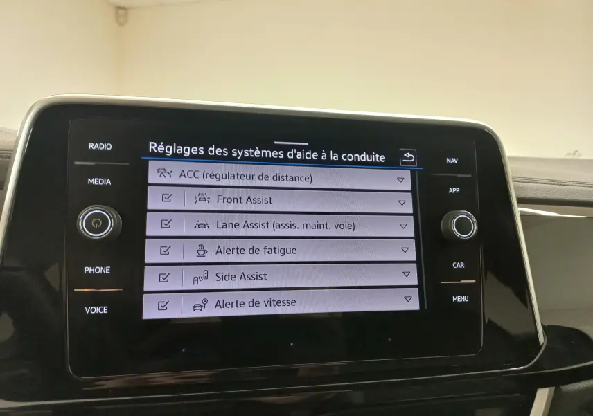 Vue rapprochée de l’écran tactile central du Volkswagen T-Roc 2025 noir intense, affichant les réglages des aides à la conduite.
