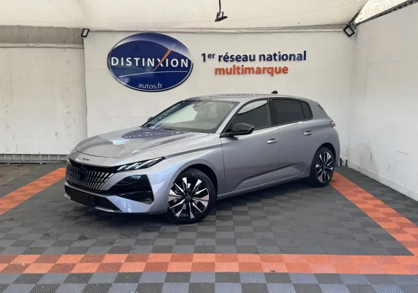 Peugeot 308 gris clair vue 3/4 avant droit, avec calandre distinctive et jantes noires et argentées.