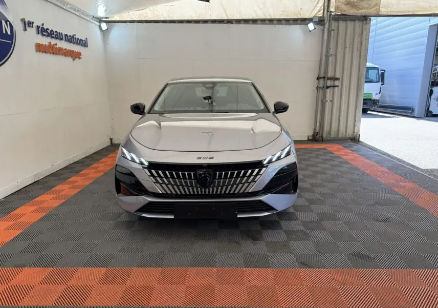 Peugeot 308 BlueHDi 130 gris clair vue de face, mettant en valeur sa calandre distinctive et ses phares LED fins.