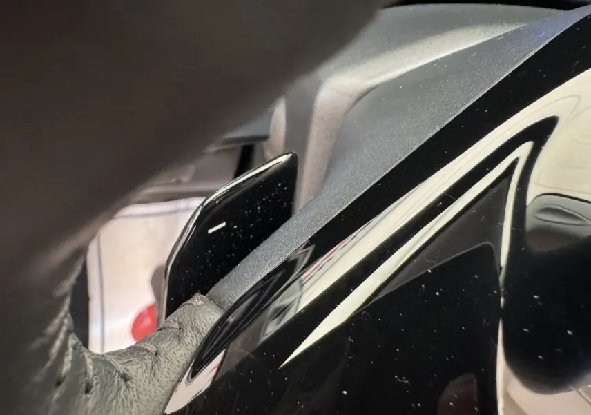 Gros plan sur le levier de palettes au volant cuir noir de la Peugeot 308 gris clair, intérieur côté conducteur.