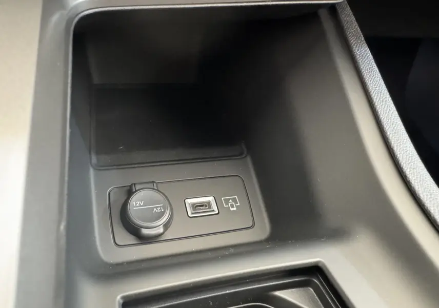 Gros plan sur la prise 12V et port USB dans le rangement central avant de la Peugeot 308 gris clair 2026.