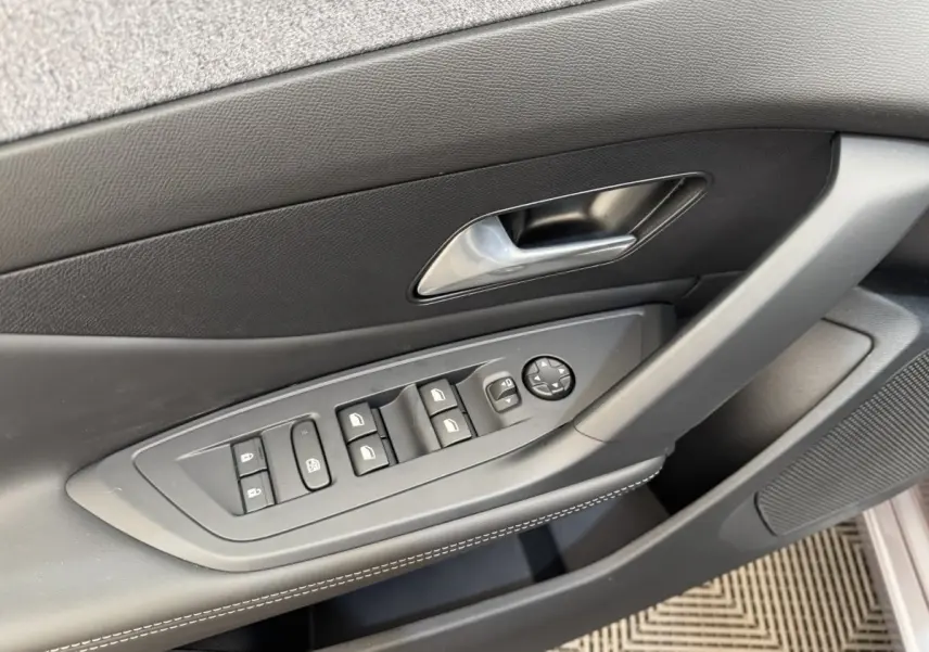 Vue rapprochée de la porte côté conducteur de la Peugeot 308 gris clair avec commandes électriques des vitres et rétroviseurs.